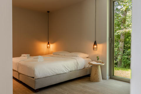 Habitación moderna en una cabaña con dos camas, lámparas colgantes y vista al bosque verde.