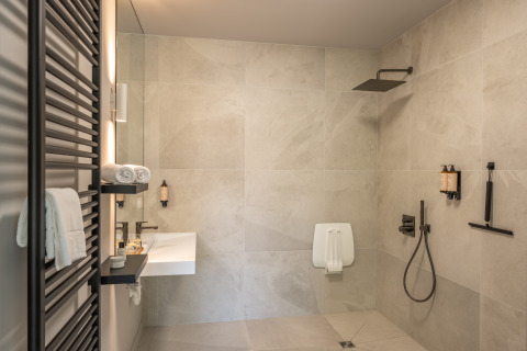 Salle de bain moderne dans un lodge avec douche à l’italienne, lavabo mural et serviettes blanches pliées.