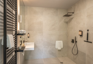 Salle de bain moderne dans un lodge avec douche à l’italienne, lavabo mural et serviettes blanches pliées.