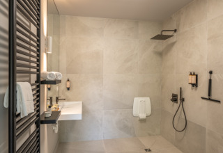 Salle de bain moderne dans un lodge avec douche à l’italienne, lavabo mural et serviettes blanches pliées.