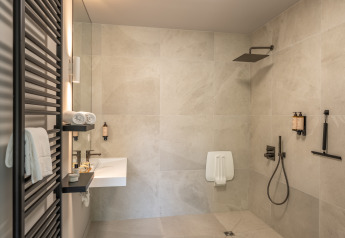 Salle de bain moderne dans un lodge avec douche à l’italienne, lavabo mural et serviettes blanches pliées.