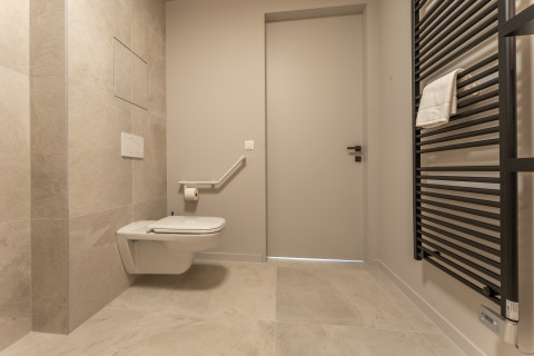 Bagno accessibile in un lodge con WC sospeso, maniglione di supporto e scaldasalviette nero a parete.