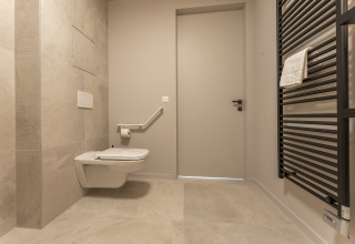 Baño accesible en un lodge con inodoro suspendido, barra de apoyo y radiador toallero negro en la pared.