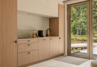 Moderne Küchenzeile aus hellem Holz mit großen Fenstern und Blick ins Grüne in einer Lodge.