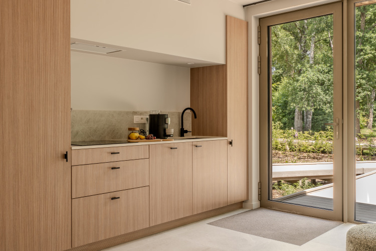 Pequeña cocina moderna de madera clara junto a un gran ventanal con vista al bosque en una cabaña.