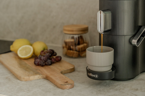 Kaffemaskine brygger kaffe på et køkkenbord med citroner, druer og sukkerterninger i baggrunden.