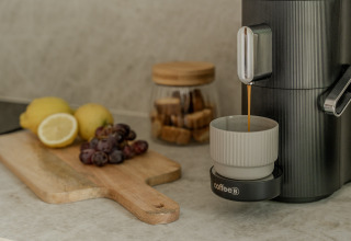 Kaffeemaschine bereitet Kaffee zu, daneben liegen Zitronen, Trauben und Zuckerwürfel im Hintergrund.