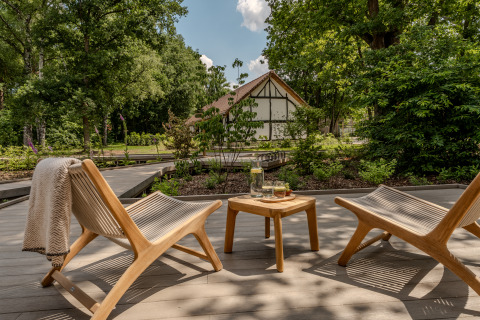 Gemütliche Terrasse mit zwei Stühlen, kleinem Tisch und Blick auf eine Lodge im grünen Garten.