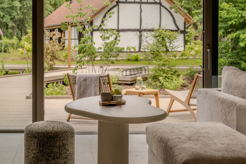 Acogedora sala de lodge con muebles modernos frente a una terraza y jardín con casa tradicional al fondo.