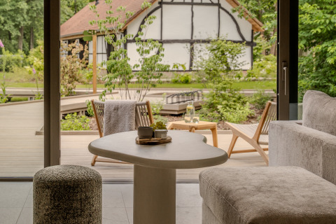Knusse lodge woonkamer met moderne meubels, zicht op terras en tuin met een traditioneel huis.