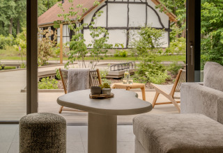 Gemütliches Lodge-Wohnzimmer mit Blick auf eine Terrasse und ein Fachwerkhaus in grüner Natur.