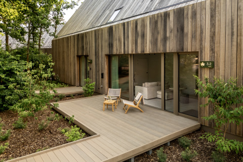 Lodge moderno con rivestimento in legno, terrazza esterna, sedie e verde in un ambiente tranquillo.