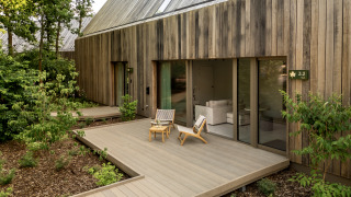 Udendørs terrasse med stole foran en moderne træhytte i naturskønne, grønne omgivelser ved en lodge.