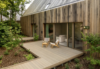 Lodge moderno con rivestimento in legno, terrazza esterna, sedie e verde in un ambiente tranquillo.