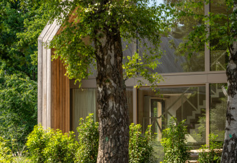 Lodge moderne aux Woodz Lodges en Belgique, grandes baies vitrées, entouré de végétation luxuriante.