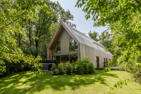Moderne lodge met jacuzzi, omringd door weelderig groene bomen en gazon, in natuurlijk daglicht.