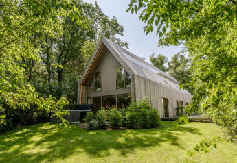 Moderne lodge met jacuzzi, omringd door weelderig groene bomen en gazon, in natuurlijk daglicht.