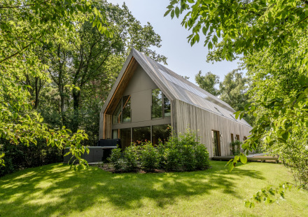 Moderne lodge met jacuzzi, omgeven door groene bomen en grasveld, verlicht door daglicht.