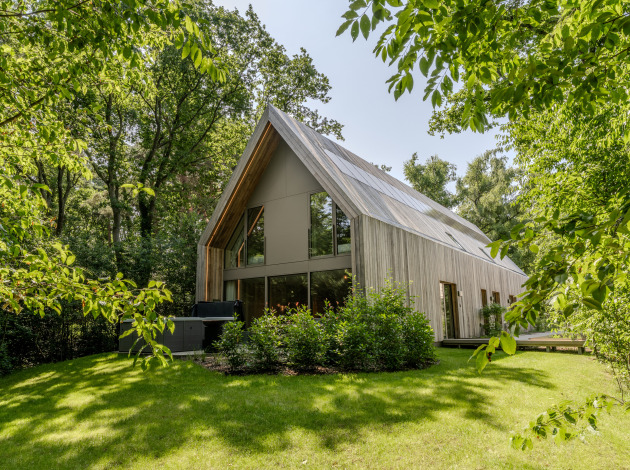 Moderne lodge met jacuzzi, omgeven door groene bomen en grasveld, verlicht door daglicht.