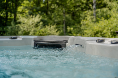 Bubbelbad buiten bij een lodge, helder bruisend water en een groene bosrijke achtergrond.
