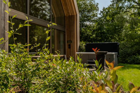 Modern lodge with large windows and outdoor jacuzzi surrounded by lush greenery at Lodge with Jacuzzi.
