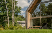 Moderne lodge met veel glas en hout, gelegen in een groene en bosrijke omgeving in het zonlicht.