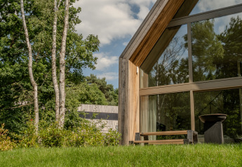Moderne lodge met veel glas en hout, gelegen in een groene en bosrijke omgeving in het zonlicht.
