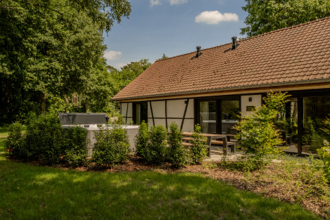 Villa Lodge met jacuzzi in de tuin, omringd door struiken, terras en een gebouw met rood pannendak.