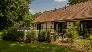Villa Lodge met jacuzzi in de tuin, omgeven door groen, buitenterras en huis met een pannendak.