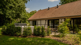 Villa Lodge met jacuzzi in de tuin, omringd door struiken, terras en een gebouw met rood pannendak.