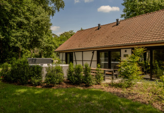 Villa Lodge met jacuzzi in de tuin, omringd door struiken, terras en een gebouw met rood pannendak.