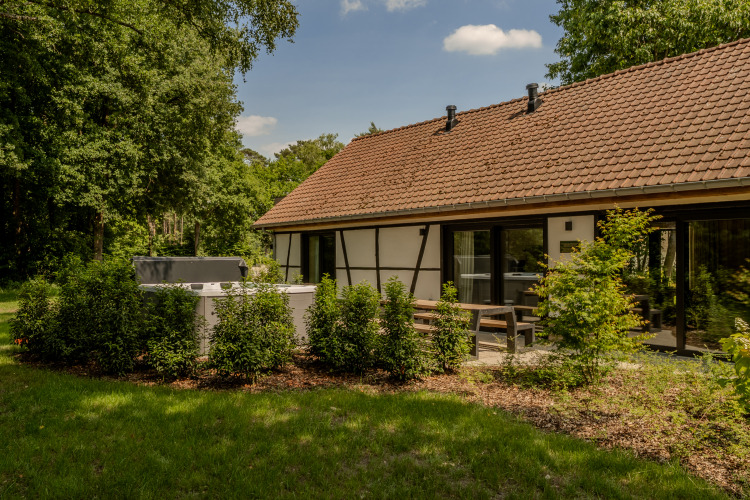 Villa Lodge mit Whirlpool im Garten, umgeben von grünen Büschen, Terrasse und Ziegeldachhaus.