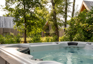 Buitenjacuzzi aan Villa Lodge bij Woodz Lodges in België, omringd door bomen en moderne chalets.