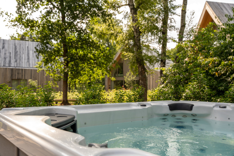 Außenwhirlpool bei der Villa Lodge in den Woodz Lodges in Belgien, umgeben von Bäumen und modernen Hütten.