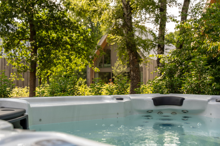 Whirlpool im Freien bei der Villa Lodge im Woodz Lodges, Belgien, umgeben von Bäumen und Natur.