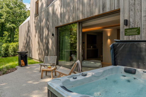 Wellness Suite lodge outdoor area with hot tub, lounge chairs, and forest surroundings for relaxation.