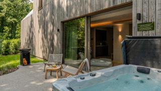 Buitenterras van Wellness Suite-lodge met bubbelbad, loungestoelen en uitzicht op het bos voor ontspanning.