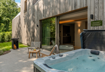 Buitenterras van Wellness Suite-lodge met bubbelbad, loungestoelen en uitzicht op het bos voor ontspanning.