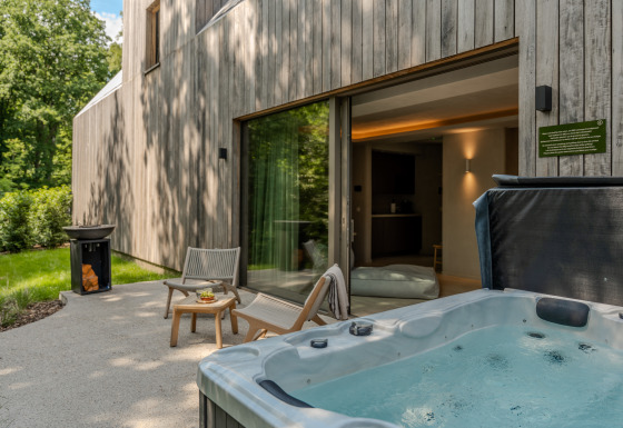 Wellness Suite lodge outdoor area with hot tub, lounge chairs, and forest surroundings for relaxation.