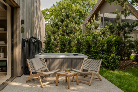 Zona de spa exterior con dos sillas y mesa en la Wellness Suite de Woodz Lodges en Bélgica, rodeada de árboles verdes.