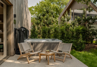 Zona de spa exterior con dos sillas y mesa en la Wellness Suite de Woodz Lodges en Bélgica, rodeada de árboles verdes.