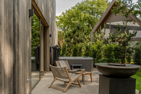 Outdoor patio at Wellness Suite in Woodz Lodges, Belgium, with chairs, table, hot tub, and fire pit.