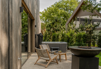 Buitenterras bij Wellness Suite van Woodz Lodges in België, met stoelen, tafel, hottub en vuurkorf.