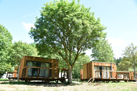 Deux cabanes en bois au lodge Cocoon de l'Ourthe, entourées d’arbres verdoyants lors d’une journée ensoleillée.