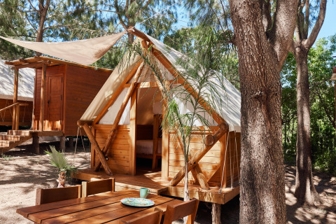 Cabina glamping in legno e tela con tavolo all'aperto tra alberi a TAIGA Tarifa, Andalusia, Spagna.