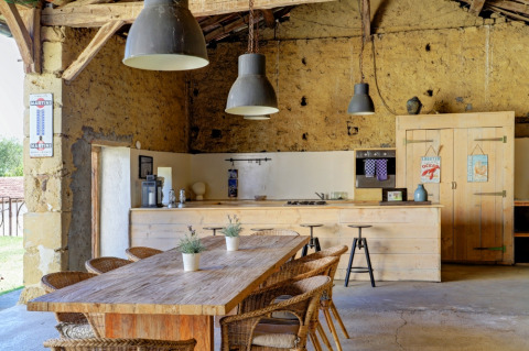Landkøkken i rustik stil med træbord, kurvestole og hængende lamper på Domaine La Barbe i Occitanie, Frankrig.