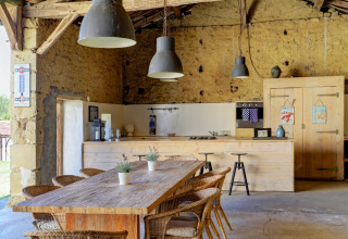 Landkøkken i rustik stil med træbord, kurvestole og hængende lamper på Domaine La Barbe i Occitanie, Frankrig.