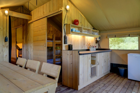 Interior de una tienda de glamping en Domaine La Barbe, Francia, con muebles de madera y cocina básica.
