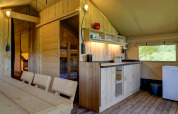 Interior de una tienda de glamping en Domaine La Barbe, Francia, con muebles de madera y cocina básica.