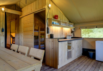 Interno di una tenda glamping al Domaine La Barbe in Francia con mobili in legno e angolo cottura.